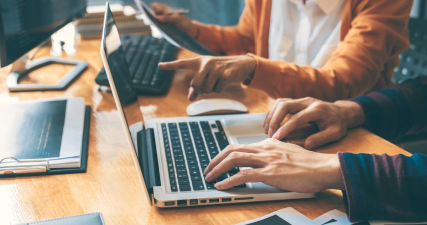 Pessoas mexendo em um notebook e uma mulher apontando para  atela de um deles