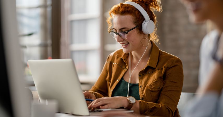 Mulher com um fone de ouvido estilo head phone e mexendo no notebook 